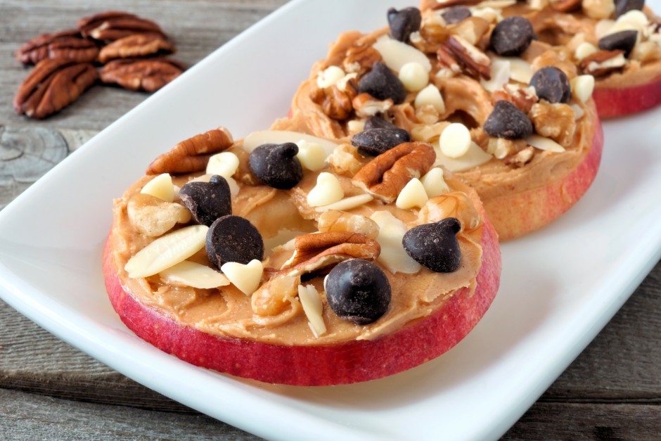Autumn apple rounds with peanut butter, chocolate chips and nuts, on white serving plate